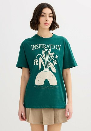 Mujer joven con una camiseta verde que tiene un diseño de un jarrón con flores y la palabra "INSPIRACIÓN" encima, combinada con una falda beige.