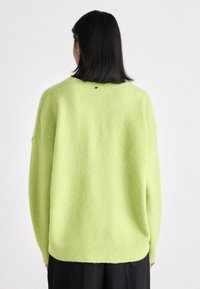 Pārmērīgs, spilgti zaļš džemperis, izgatavots no mīksta adījuma materiāla, ar apaļu kakla izgriezumu un ribotām malām, ar mazu logotipa detaļu aizmugurē.