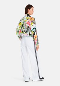 Colorful track jacket with a tropical print, paired with white pants featuring black stripes along the sides. Smooth fabric and relaxed fit.