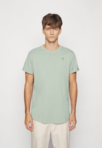 T-shirt en coton vert menthe avec un col rond, des manches courtes et un logo discret sur la poitrine. Texture lisse, coupe décontractée.