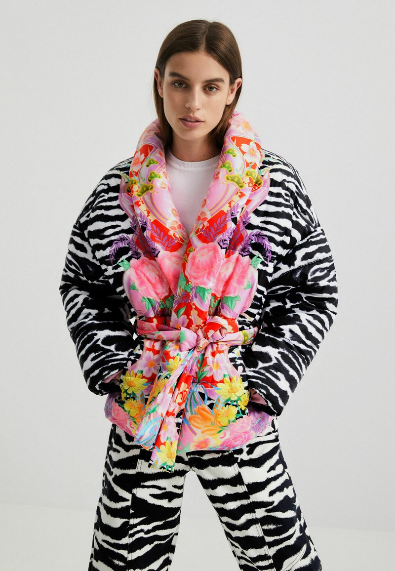 Puchowa kurtka w paski zebry z żywym, kwiatowym kołnierzem i paskiem. Cechuje się mieszanką intensywnych kolorów i faktur.