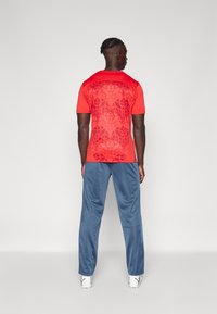 Rood shirt met korte mouwen en een subtiel patroon, gecombineerd met blauwe broeken. Het heeft een ronde halslijn en een aansluitende pasvorm.