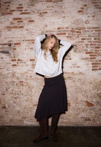 Jasnoszara krótka bluza, granatowo-czarna spódnica midi w paski z asymetrycznym dołem, zestawiona z brązowymi zamszowymi kozakami za kolano.