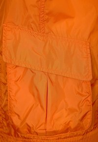 Orange vadderat tyg med en ficka med lock, slät textur och samlad elastisk midja för en säker passform.