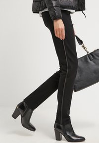Černé tailored kalhoty slim fit s bočním pruhem. Kombinované s černými kotníkovými botami a texturovanou černou kabelkou.