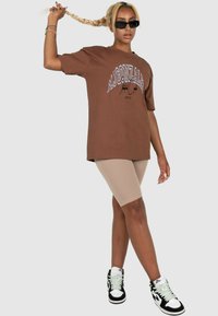 Brown oversized t-shirt with graphic text, paired with beige cycling shorts and black high-top sneakers with white and mint accents.