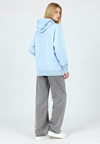 Felpa azzurra chiara con cappuccio regolabile, vestibilità comoda, polsini a coste, abbinata a pantaloni ampi grigi chiari e scarpe bianche.