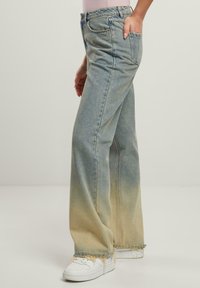 Jeans de mezclilla azul claro con un diseño acampanado, que presentan un efecto ombré de azul a beige claro, dobladillo deshilachado y bolsillos estándar.