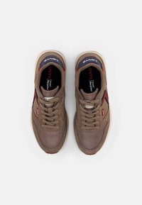 Brązowe buty sportowe z siateczkowego i zamszowego materiału, z czerwonymi i granatowymi akcentami, sznurowadłami i teksturowaną podeszwą. Logo marki widoczne wewnątrz.
