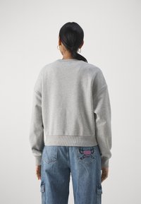Felpa grigia chiara con collo e polsini a costine; esposta con pantaloni in denim larghi dotati di un logo ricamato rosa sul retro.