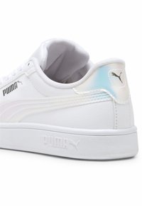 Sneakers bianchi Puma con una finitura in pelle liscia, con linguetta sul tallone iridescente e suola in gomma bianca. Presenta il logo argento sul lato e sul tallone.