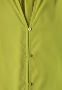 Gros plan d'un chemisier vert citron avec trois petits boutons assortis et un col en V.