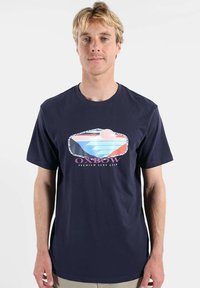 T-shirt en coton bleu marine à manches courtes, avec un graphique coloré représentant des vagues et un soleil, accompagné du texte « Oxbow Premium Surf Gear » sous l'image.