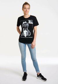 Black cotton t-shirt featuring a graphic of a furry character in a tuxedo, with white text and design elements. Paired with light blue skinny jeans.