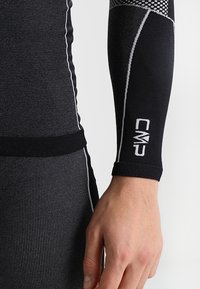 Maglietta a maniche lunghe nera in tessuto compressivo con accenti bianchi, caratterizzata da motivi testurizzati e un logo sul polsino. Design morbido, elastico e aderente.