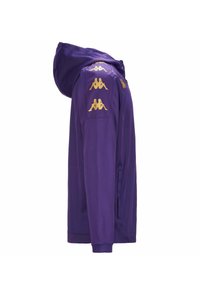 Giacca viola con cappuccio e loghi Kappa dorati sulle spalle, texture liscia e una tasca con zip laterale. Caratterizza un design atletico moderno.
