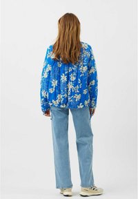 Quiltet jakke i lys blå med hvide blomster mønstre, med et afslappet fit, ribstrikkede manchetter og justerbare snore ved kanten. Sættes sammen med lyse denim jeans.