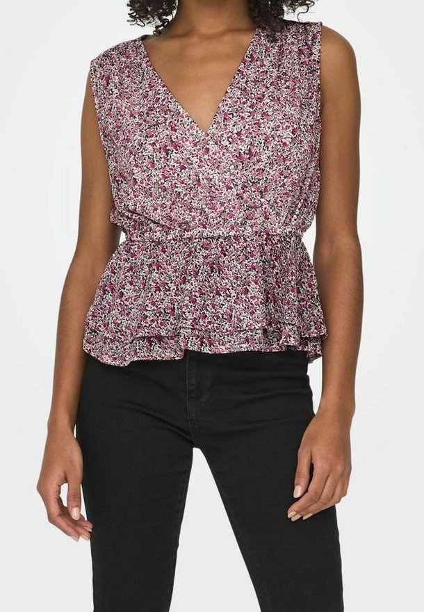 Femme portant un top sans manches à motif floral rose, blanc et noir avec basque, associé à un pantalon noir ajusté.