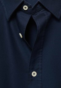 Camicia blu navy con design a colletto, caratterizzata da una patta con bottoni e tessuto testurizzato. Due bottoni di colore chiaro vicino al colletto.