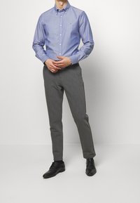 Camicia azzurro chiaro con bottoni, pantaloni grigi su misura e scarpe eleganti nere. Presenta un piccolo logo sulla camicia, una texture liscia e una vestibilità slim.