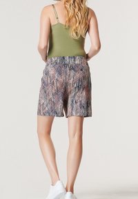 Pantaloni corti multicolore con un motivo testurizzato, dotati di una vita elastica e di una vestibilità ampia, abbinati a un top aderente color oliva e sneakers bianche.