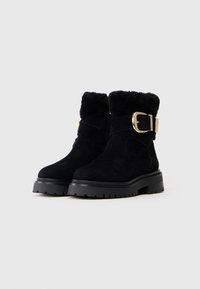 Botine negre din suede, cu tălpi din cauciuc masiv, mansetă din blană sintetică și detalii cu catarame mari aurii pe curelele din jurul gleznelor.