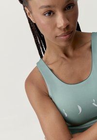 Top deportivo verde claro con escote redondeado, textura suave y diseño impreso en el pecho. Cuenta con tirantes anchos y una silueta ajustada.