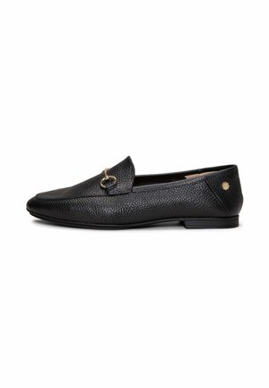 Mocasín de cuero negro texturizado con detalle de hebilla de metal dorado en la parte superior y pequeño emblema dorado cerca del talón, suela plana, estilo sin cordones.
