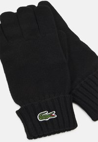 Sorte strikkede hansker med ribbestrikket mansjett og en grønn brodert krokodillelogo på håndleddet. Myk tekstur som sikrer varme og komfort.