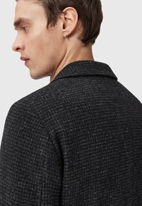 Mörk texturerad blazer med houndstooth-mönster, som har en sjalkrage och enstaka knappstängning. Tillverkad av ullblandad tyg.