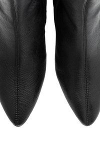 Primer plano de botas de cuero negro puntiagudas con un patrón de piel de serpiente texturizado y costuras visibles a lo largo del centro delantero.