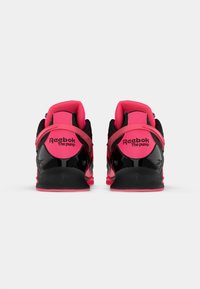 Čierne a ružové Reebok tenisky s vysokým strihom. Medzi vlastnosti patrí textúrovaný čierny zvršok, ružové akcenty a viditeľné logo na päte.