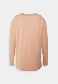 Koszula z długim rękawem w jasnoskalnym kolorze brzoskwiniowym z okrągłym dekoltem, zaokrąglonym dołem i luźnym krojem. Gładka textura i minimalne detale w szyciu.