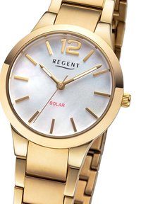 Montre en acier inoxydable doré avec un boîtier rond, un cadran en nacre blanche, des index horaires dorés et le texte rouge "SOLAR". Bracelet à maillons ajustable.