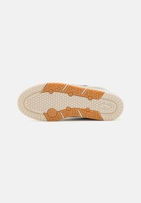 Suela de zapatilla con un diseño texturizado que presenta un patrón de panal, en colores beige y naranja, material de goma y surcos de tracción distintivos.