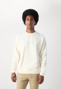Sweatshirt i blød cremefarvet stof med rund hals, ribbede manchetter og et diskret "Scotch & Soda" logo i lys brun på brystet.