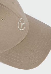 Tan baseball cap lavet af tekstureret stof, med et broderet hvidt Mercedes-logo foran. Bøjet skygge med tydelige syningslinjer.