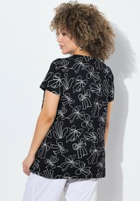 Camiseta de manga corta negra con un diseño de arte lineal en blanco de lazos y cintas. Tejido suave con un corte holgado, adecuado para un uso casual.