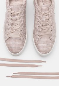Blush pink sneakers with textured crocodile pattern, smooth fabric, and flat laces. Features a rounded toe and rubber sole.