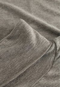 Pelēka auduma ar gludu tekstūru, kas iezīmējas ar piekārtajām krokām. Smalkas krāsu variācijas radījušas maigu, nedaudz blāvu izskatu.