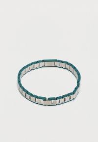 Βραχιόλι από ασημί και σκούρο πράσινο μέταλλο με ορθογώνια κομμάτια και χαραγμένο λογότυπο «Lacoste» σε ανοιχτό φόντο.