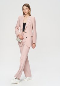 Jasnoróżowy dopasowany żakiet i pasujące spodnie, z dwoma przednimi kieszeniami i czarnymi guzikami. Noszony na czarną krótką bluzkę, do tego białe trampki.