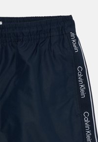 Shorts de bain bleu marine en tissu léger, dotés d'une taille élastique et de bandes blanches sur les côtés avec le texte "Calvin Klein".