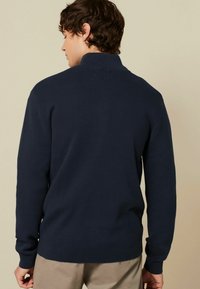 Marineblauer Strickpullover mit hohem Kragen, langen Ärmeln und gerippten Bündchen. Glatte Textur ohne Muster, gestaltet in einer taillierten Form.