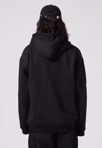 Black hoodie with a drawstring hood, loose fit, and textured fabric. Complemented by a black cap with an adjustable strap.