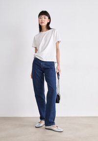 Bela bombažna majica, sproščen kroj; temno modri ravni jeans; srebrni balerinki; črna torbica s kovinskim ročajem; minimalistična ozadja.