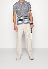 Kortärmad åtsittande skjorta med blå och grå horisontella ränder, tillsammans med beige rutiga byxor. Slät tyg, modern design och lätta skor.