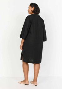 Abito nero, lunghezza al ginocchio, con colletto e maniche tre quarti. Presenta spacco laterale e una vestibilità rilassata, realizzato in un tessuto leggero e testurizzato.
