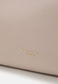 Záběr na béžovou texturovanou kůži se zlatým logem "kate spade NEW YORK" umístěným ve středu povrchu.