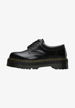 Zwarte leren veterschoen met een dikke, getande zwarte rubberen zool en gele stiksels langs de rand, met een gladde afwerking.